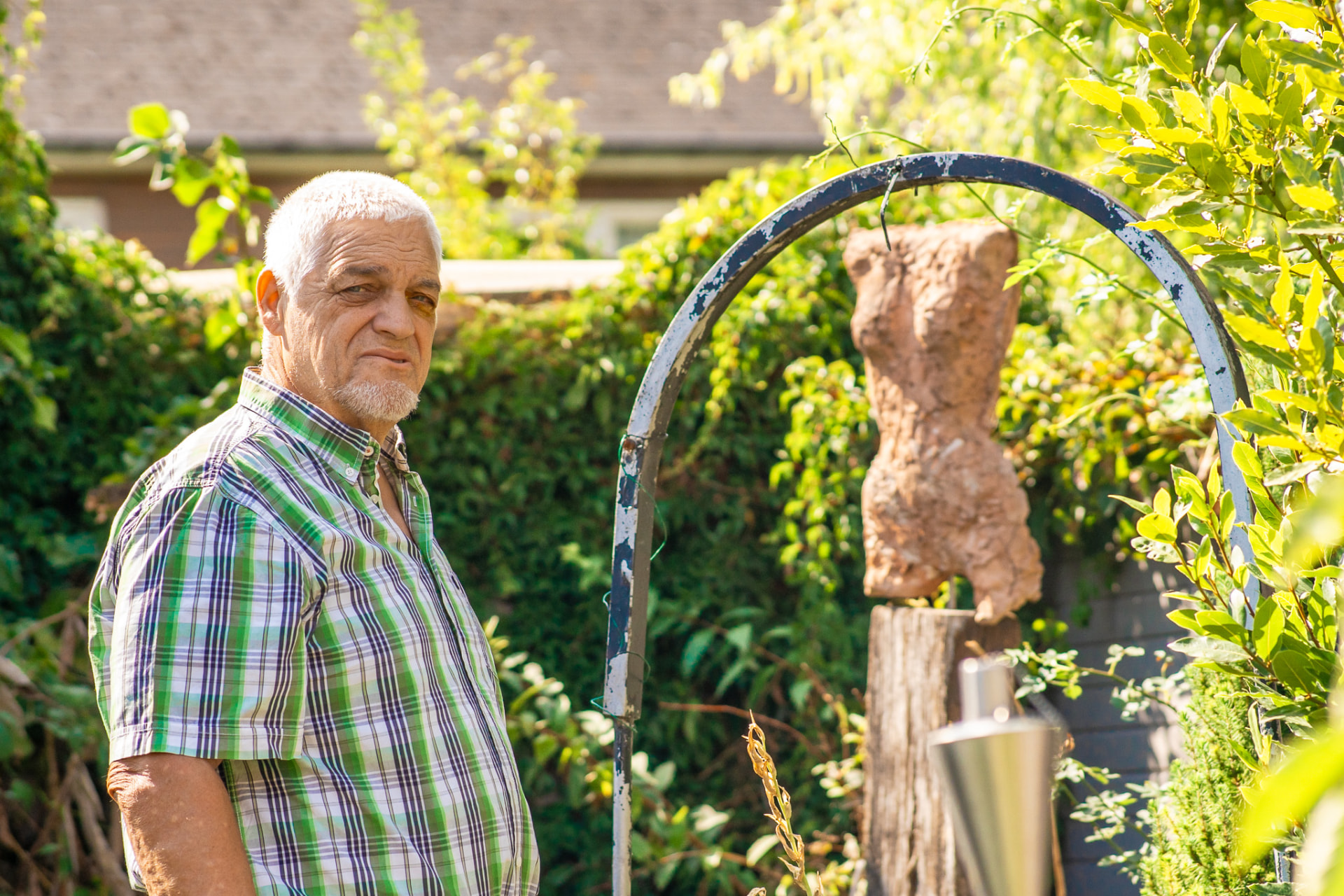 Portret van een man in een geruit hemd in een tuin met sculptuur